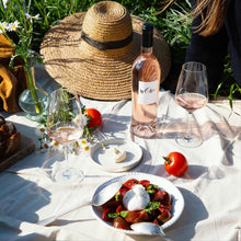 Load image into Gallery viewer, Outdoor picnic setup with a bottle of BY-OTT Provence Rose wine, food, and a straw hat on a sunny day.