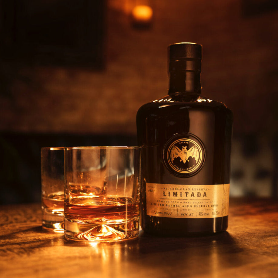 Bottle of Bacardi-Gran-Reserva-Limitida-Rum with two glasses on a wooden surface in a dimly lit setting