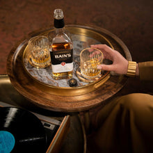 Load image into Gallery viewer, Bottle of Bains Grain whiskey with two glasses on a wooden tray, with a person holding one glass.