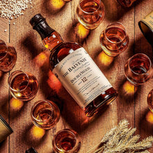 Load image into Gallery viewer, Balvenie 12 year old whiskey bottle and glasses on a wooden surface with grain and wheat accents.