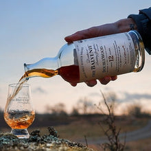 Load image into Gallery viewer, Person pouring Balvenie 12 year old whisky into a glass with a scenic background