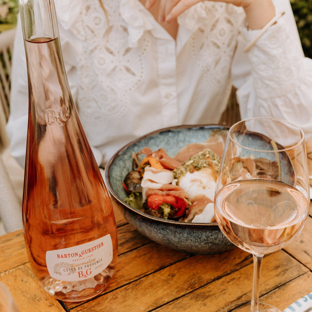 Bottle and glass of rosé wine on a wooden table with food