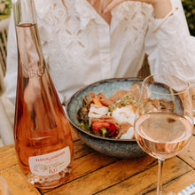 Load image into Gallery viewer, Bottle and glass of rosé wine on a wooden table with food