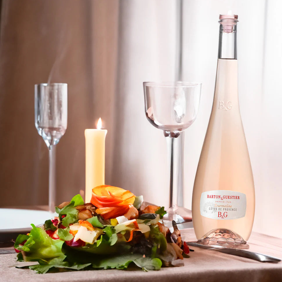 Bottle of Barton & Guestier rosé wine with a candle and salad on a table.
