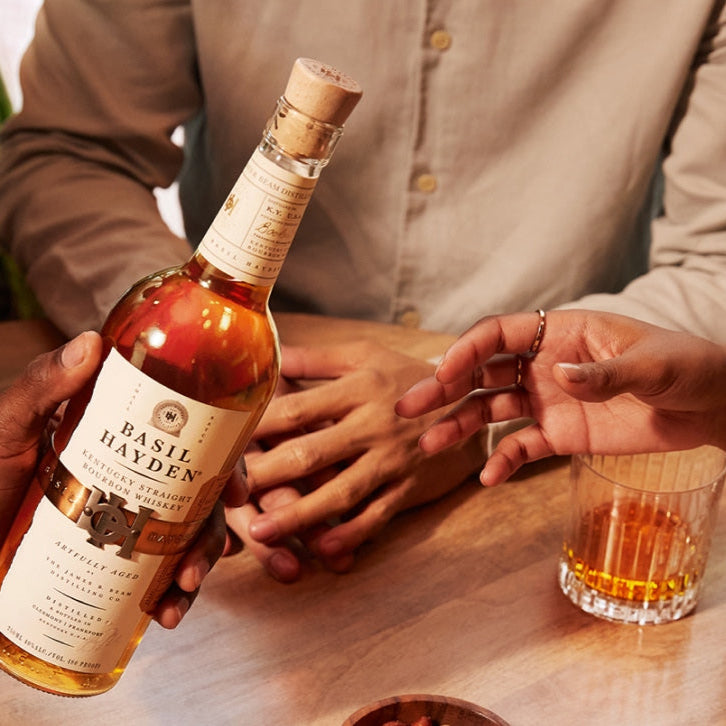 Load image into Gallery viewer, Person holding a bottle of whiskey with a glass at a table.