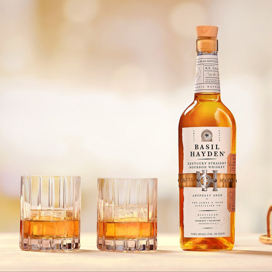 Load image into Gallery viewer, Bottle of whiskey and two glasses on a table with a blurred background.