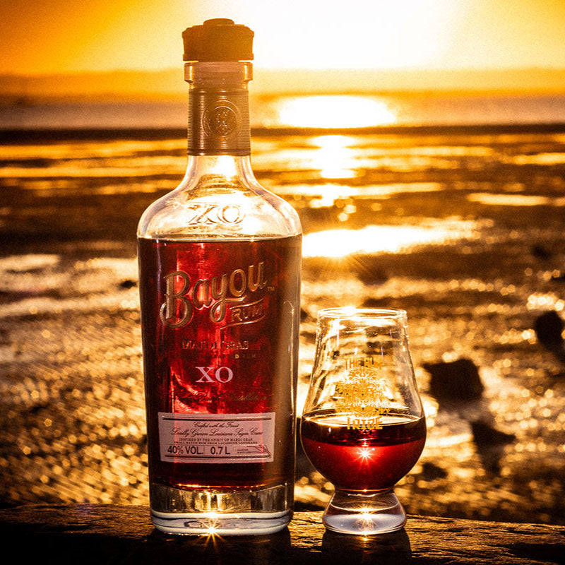 Bottle OF Bayou XO Mardis Gras Rum with a sunset over water background