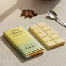 Load image into Gallery viewer, Lemon white chocolate bar with packaging on a light surface, surrounded by almonds and a spoon.