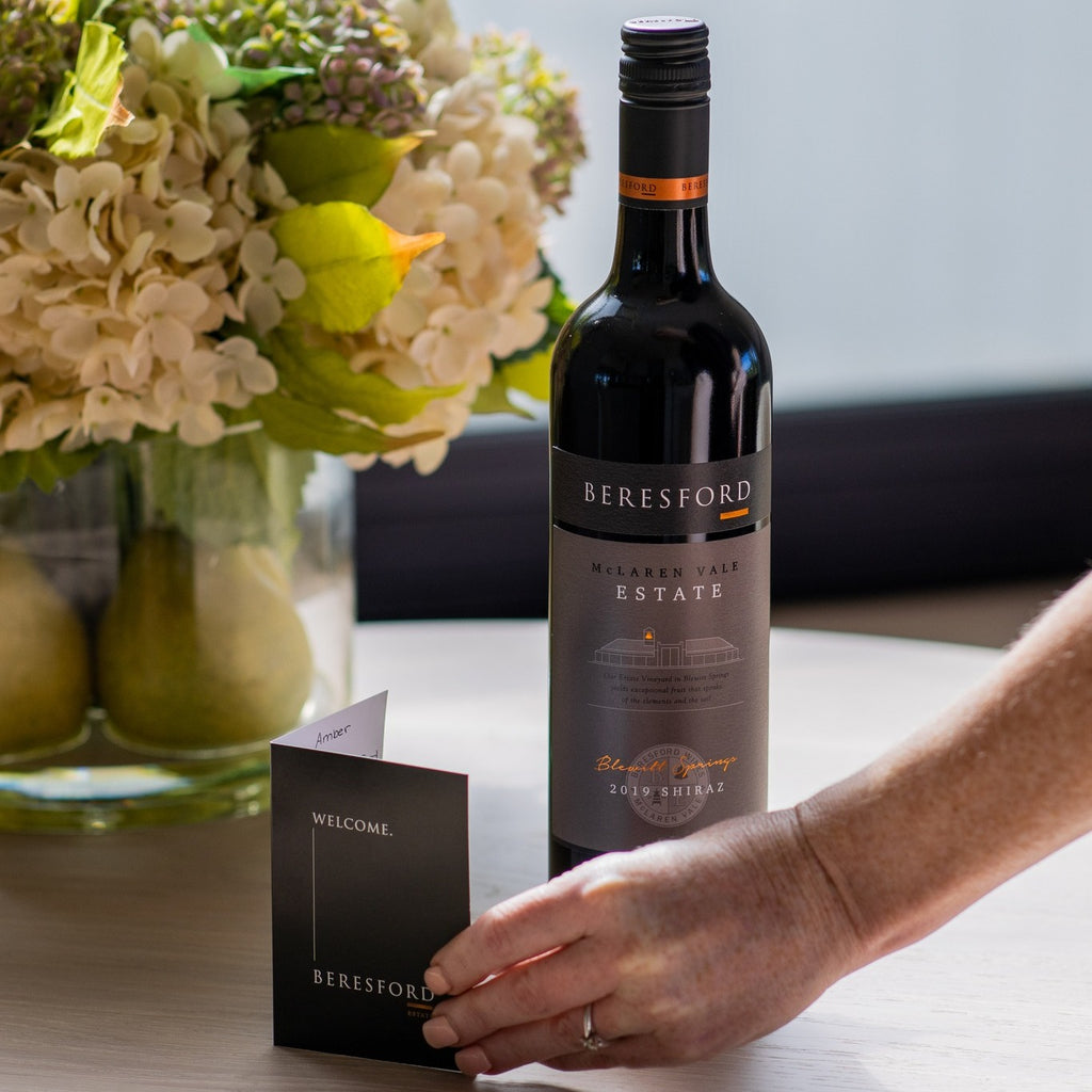 Beresford McLaren Vale Estate Shiraz wine bottle with a hand holding a card on a table with flowers in the background