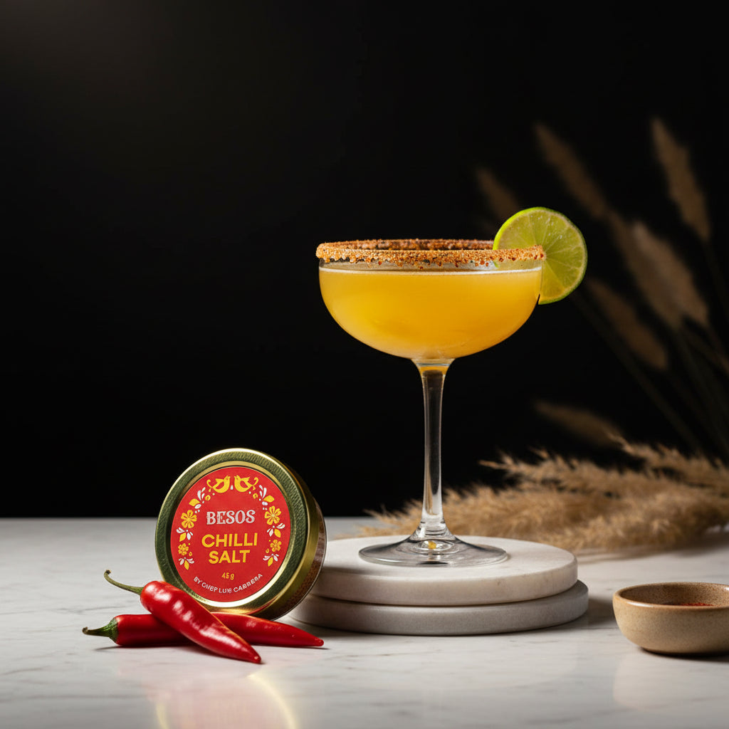 Load image into Gallery viewer, Cocktail with lime wedge and a jar of Besos Chilli Salt by Chef Luis Cabrera on a dark background