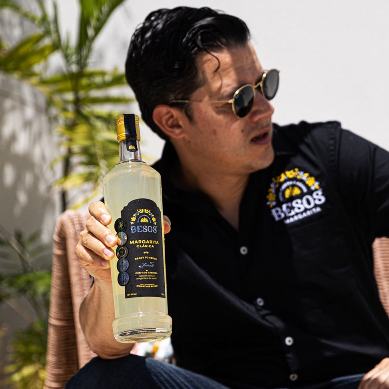 Load image into Gallery viewer, Man holding a bottle of Besos Margarita Clasica ready to serve cocktail with a plant in the background