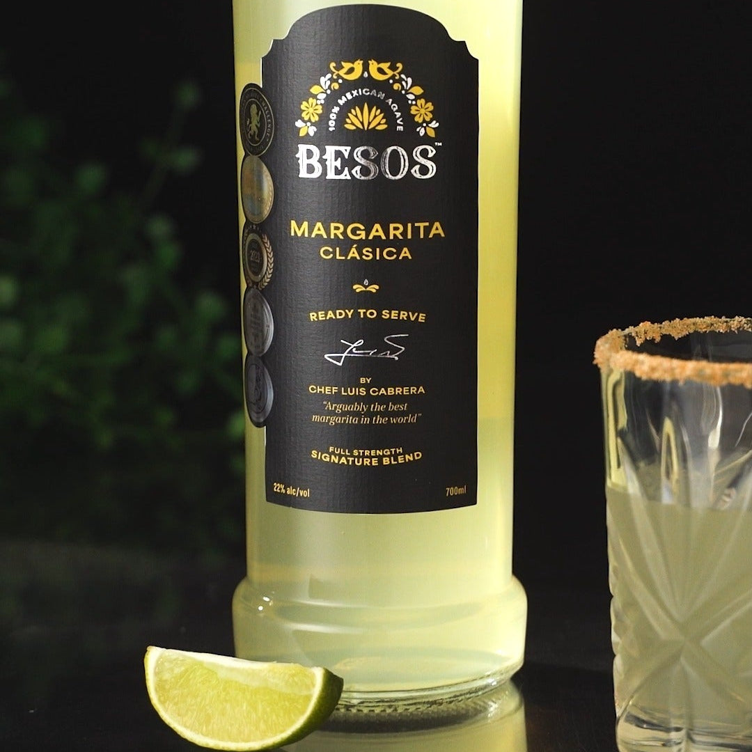 Load image into Gallery viewer, Bottle of Besos Margarita Clasica ready to serve cocktail with a lime wedge on a dark background
