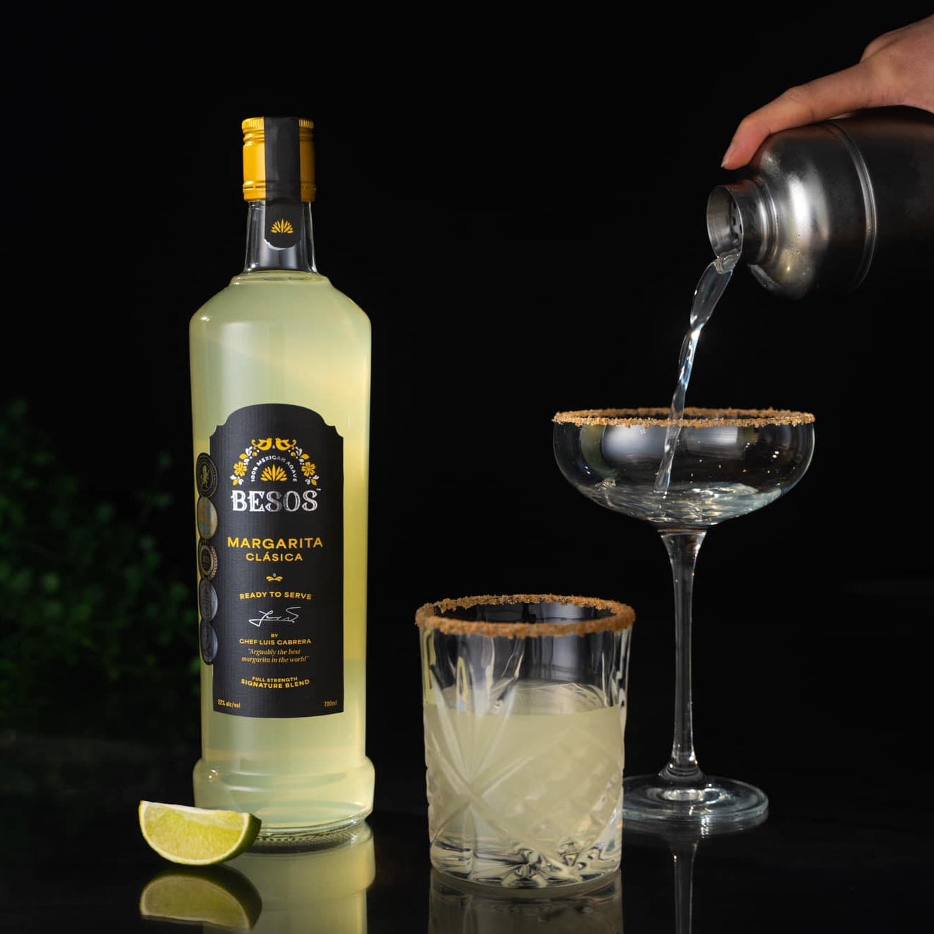 Load image into Gallery viewer, Besos margarita clasica bottle with two glasses and a lime wedge on a dark background