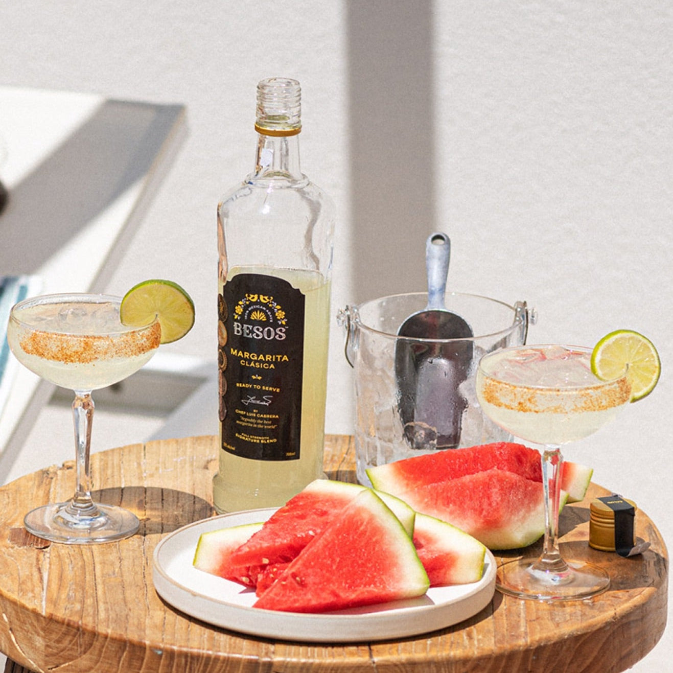 Load image into Gallery viewer, Bottle of Besos Margarita Clasica ready to serve cocktail on a wooden table with watermelon slices and cocktails.