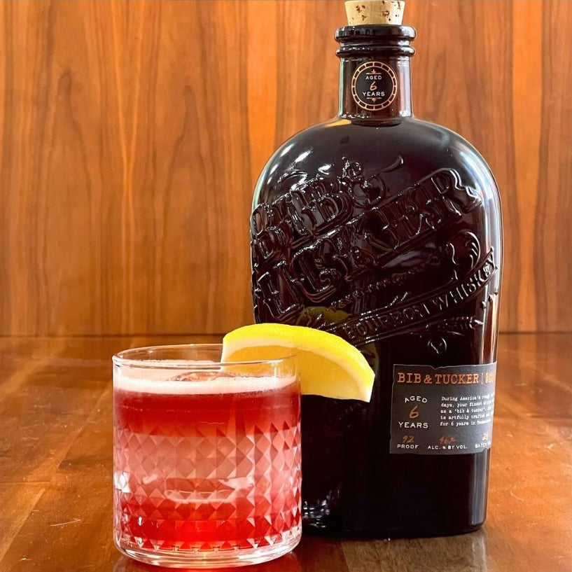 Load image into Gallery viewer, Bottle of Bib &amp; Tucker 6YO Bourbon Whiskey and a cocktail with a lemon wedge on a wooden background
