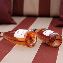 Load image into Gallery viewer, Two BIJOU LUMEA ROSÉ wine bottles on a striped surface with pillows in the background