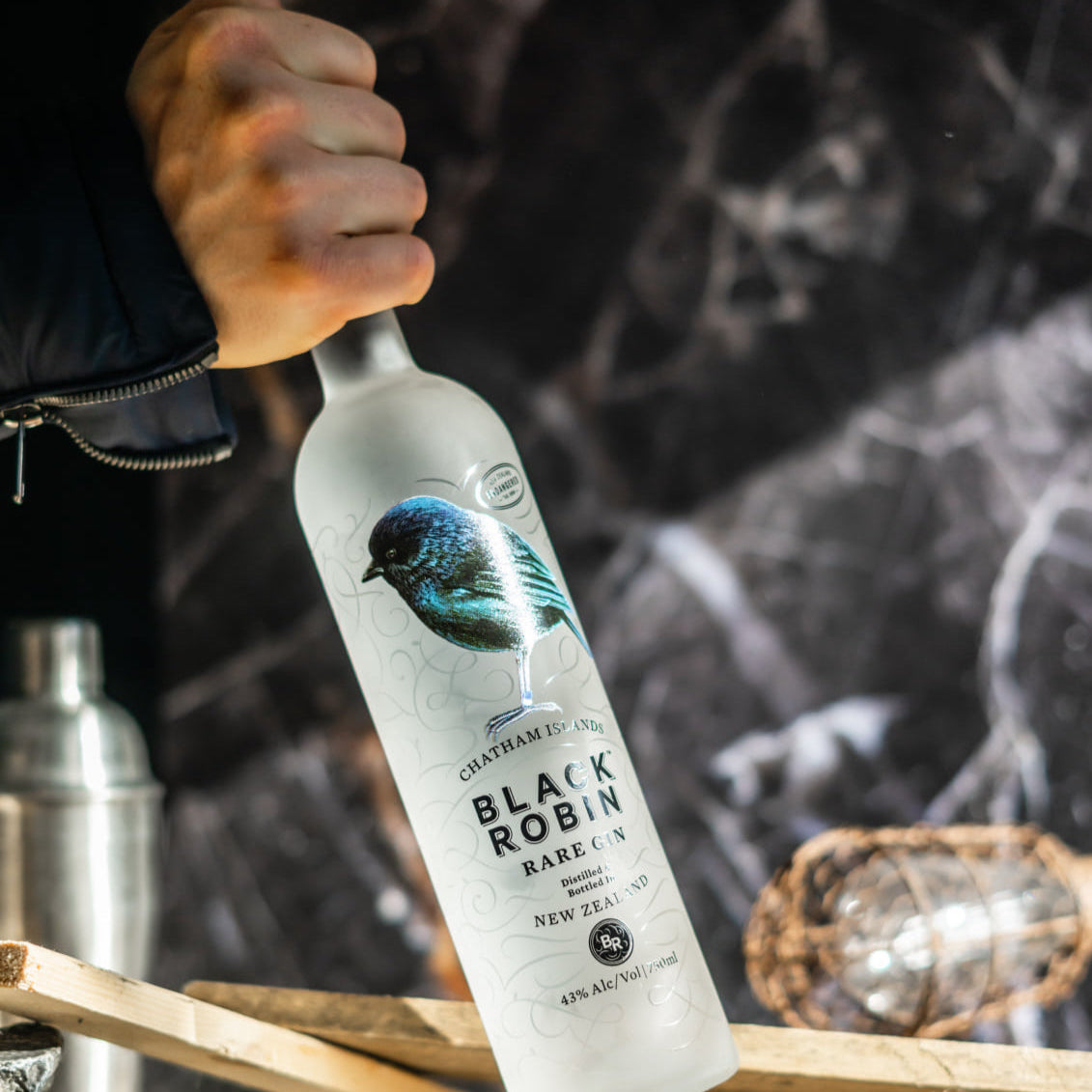 Load image into Gallery viewer, Bottle of Black Robin Rare Gin held by a person with a blurred background