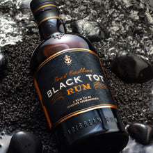 Load image into Gallery viewer, Bottle of Black Tot Rum on a dark, textured surface with ice cubes.