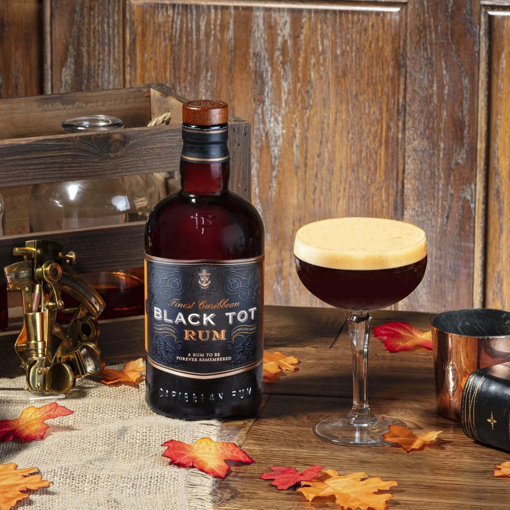Bottle of Black Tot Rum on a wooden table with a cocktail glass and autumn leaves.