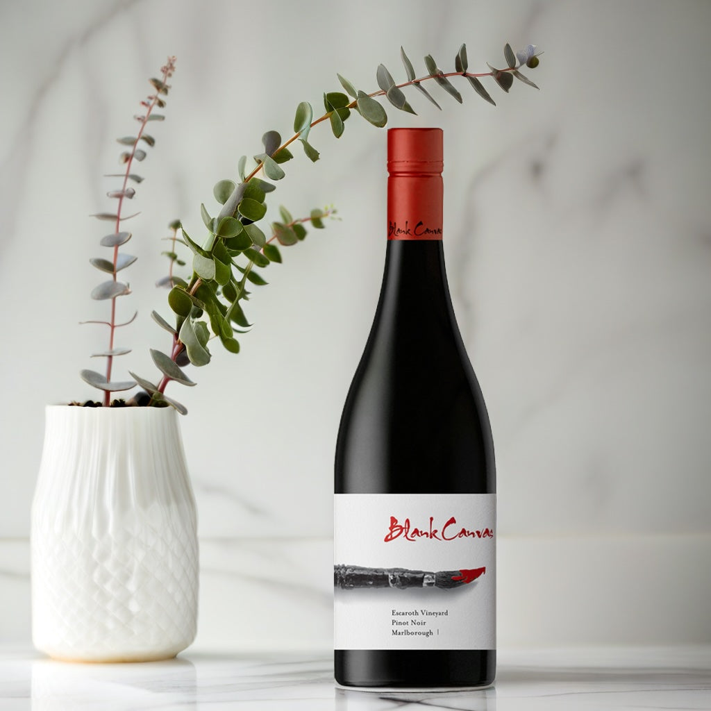 Load image into Gallery viewer, Wine bottle with a red label next to a white vase with greenery on a light gray background