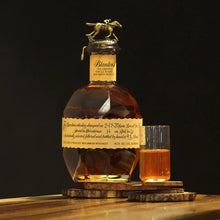 Load image into Gallery viewer, Bottle of Blanton&#39;s bourbon whiskey with a glass on a wooden coaster against a dark background