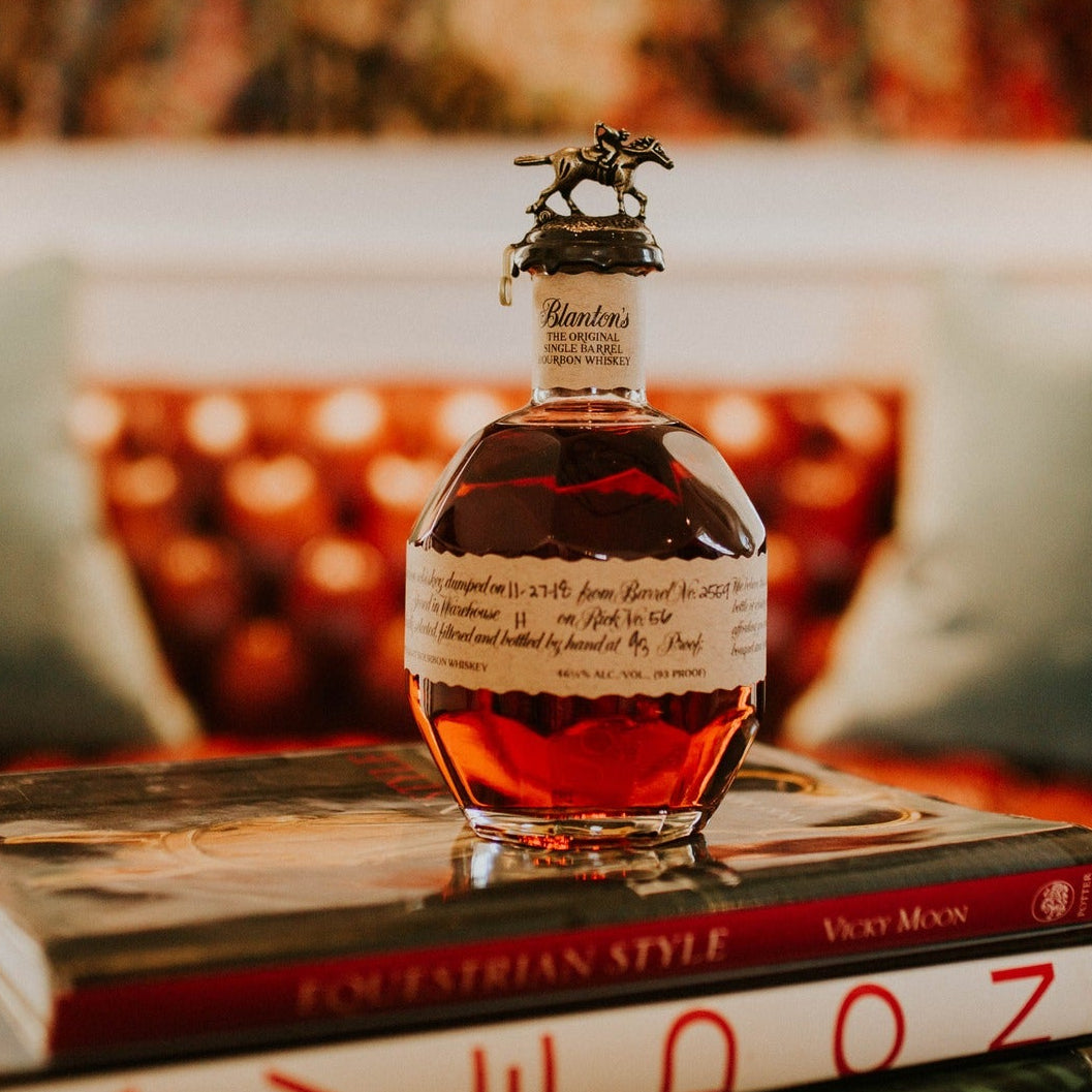 Load image into Gallery viewer, Bottle of Blantons Original Bourbon whiskey on a stack of books with a blurred background