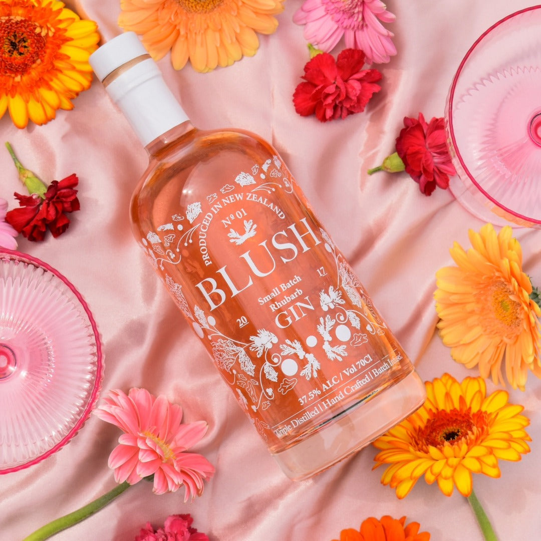 Load image into Gallery viewer, Bottle of Blush Gin surrounded by colorful flowers on a pink fabric background