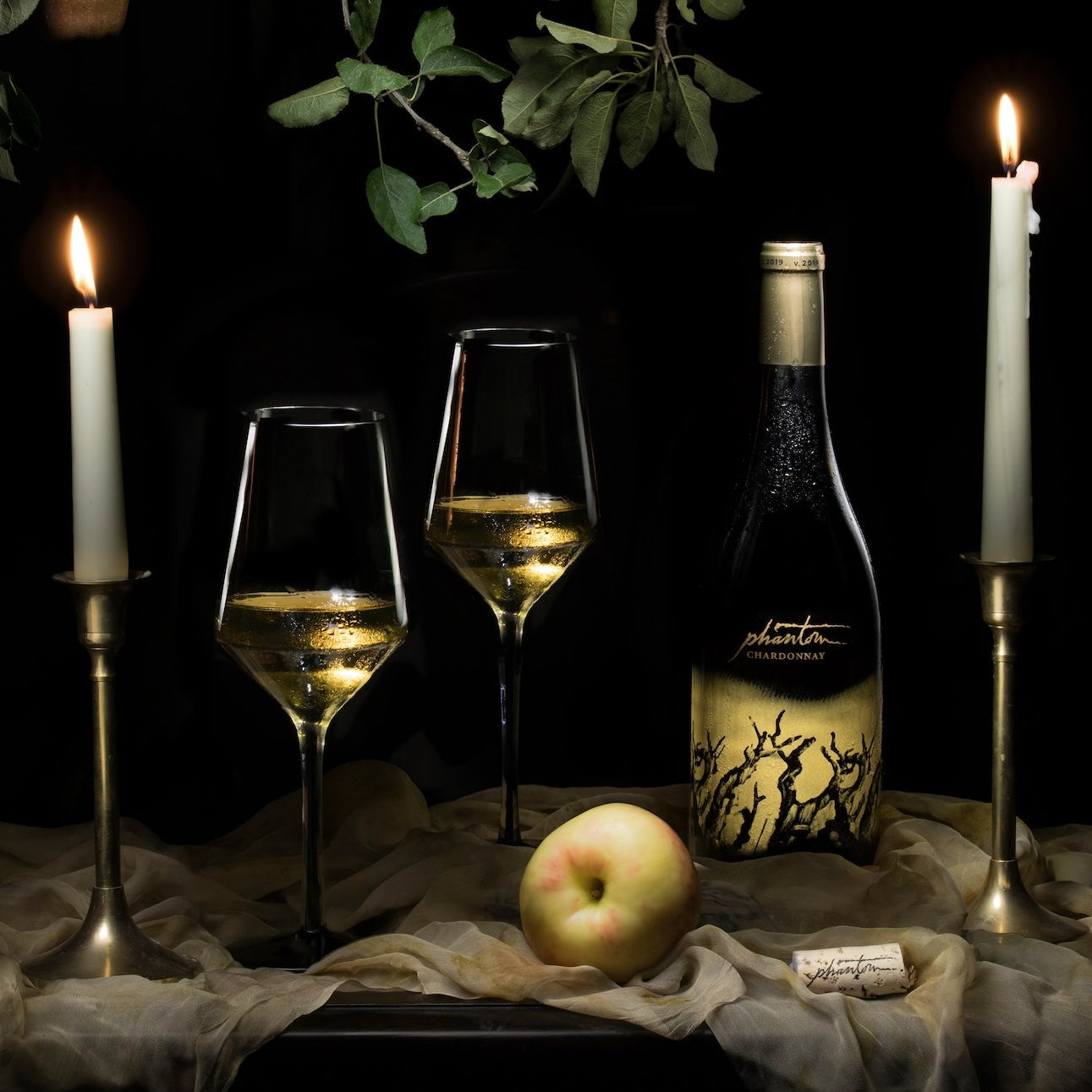 Load image into Gallery viewer, A bottle of Bogle Phantom Chardonnay two glasses of wine and candles on a table on a dark background with some leaves