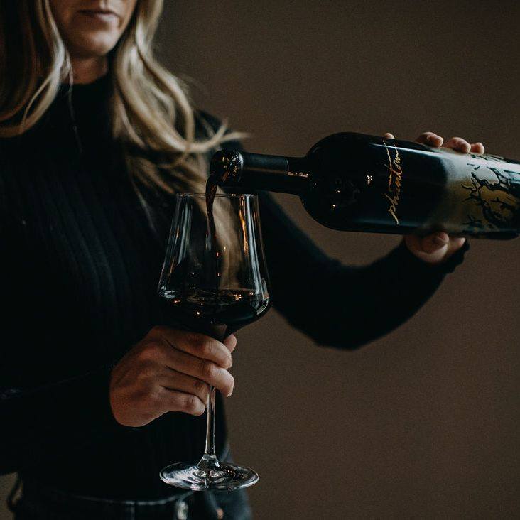 Load image into Gallery viewer, A woman pouring a bottle of Bogle Phantom Proprietary Red Blend Wine into a large wine glass