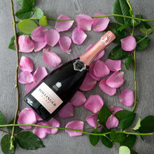 Load image into Gallery viewer, Bollinger champagne bottle surrounded by pink petals and green leaves on a gray surface