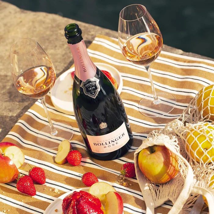 Load image into Gallery viewer, Bollinger rosé champagne bottle with two glasses on a striped cloth by a body of water.