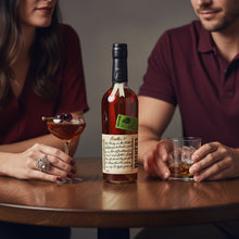 Load image into Gallery viewer, Two people sitting at a table with a bottle of Bookers-Bourbon-The-Lumberyard-Batch-Whiskey and glasses.
