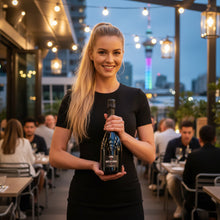 Load image into Gallery viewer, Woman holding a bottle of Bortolin Angelo Valdobbiadene Brut Prosecco in an outdoor restaurant setting with city skyline in the background