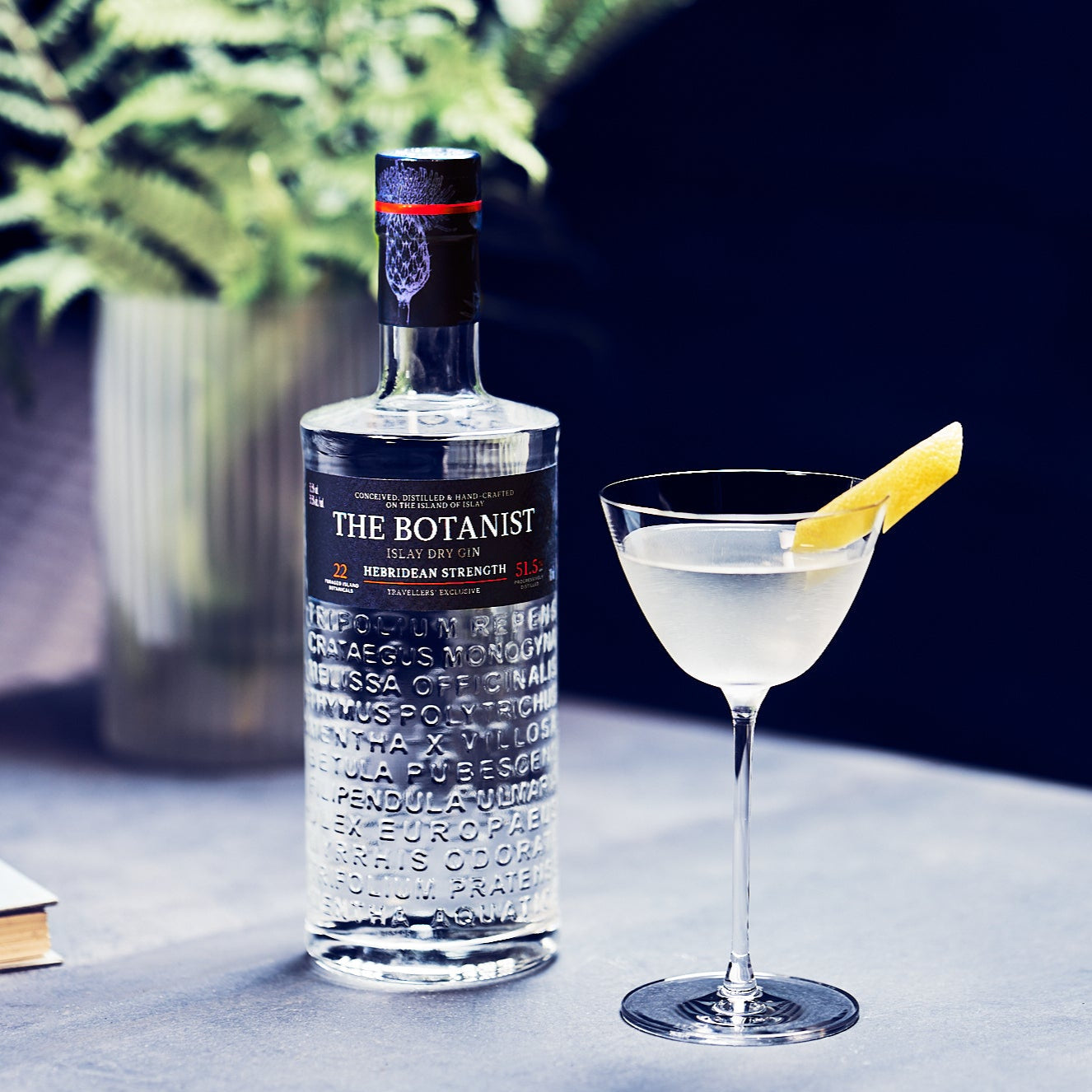 Load image into Gallery viewer, Bottle of The Botanist Hebridean Strength gin with a cocktail glass containing a lemon twist on a table.