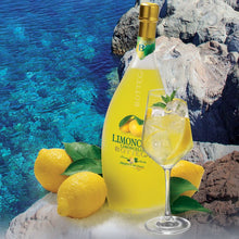 Load image into Gallery viewer, Bottle and glass of Limoncello with lemons by a rocky coastline