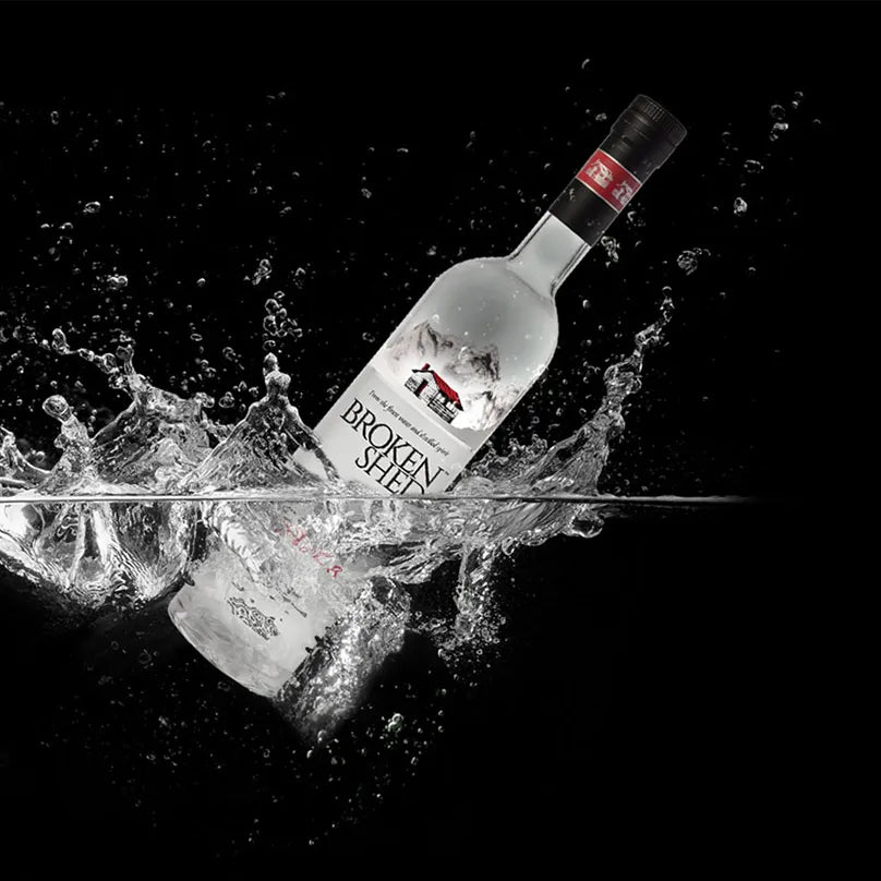 Load image into Gallery viewer, A clear glass bottle of Broken Steel vodka is shown diagonally with a dramatic splash of water around it against a solid black background.