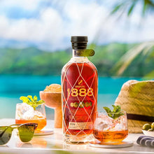 Load image into Gallery viewer, Brugal 888 rum bottle with cocktails and a hat on a tropical setting