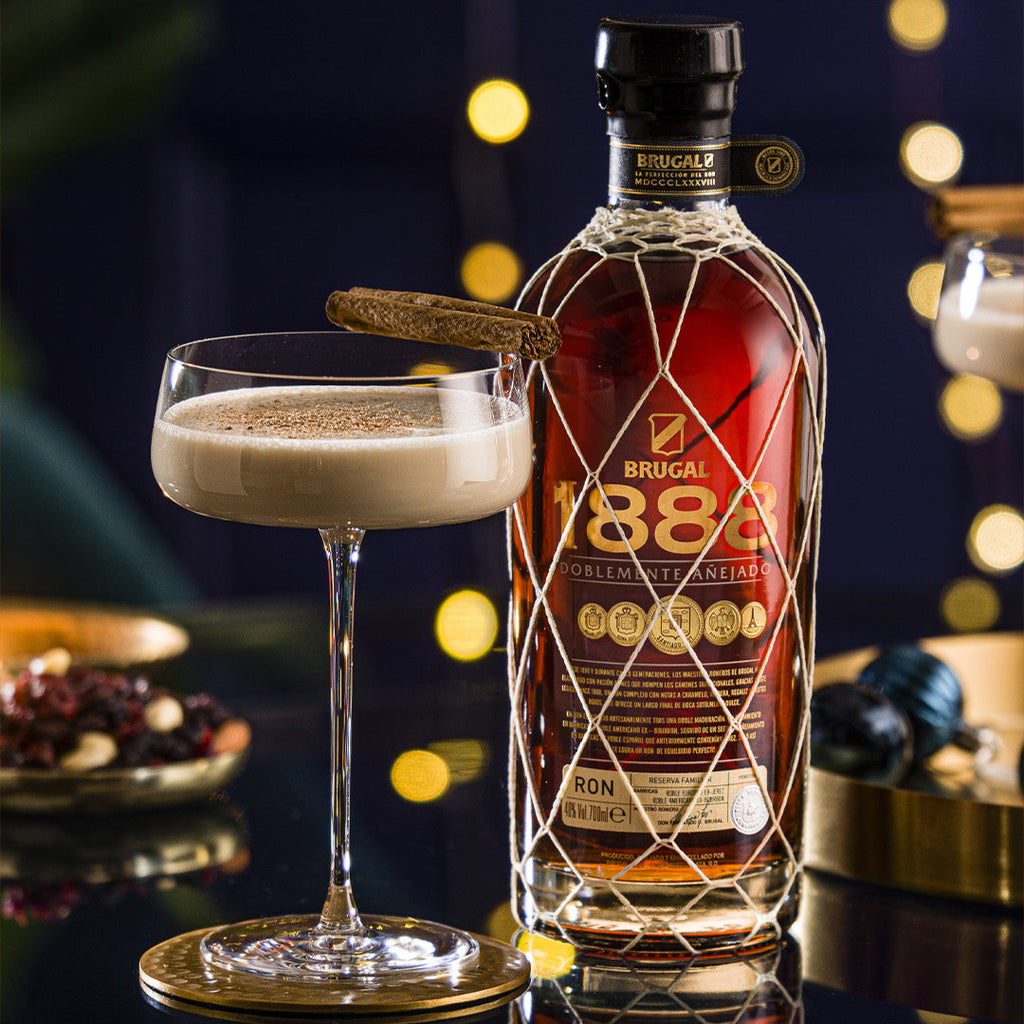 Bottle of Brugal 1888 rum with a cocktail glass on a reflective surface with blurred lights in the background.