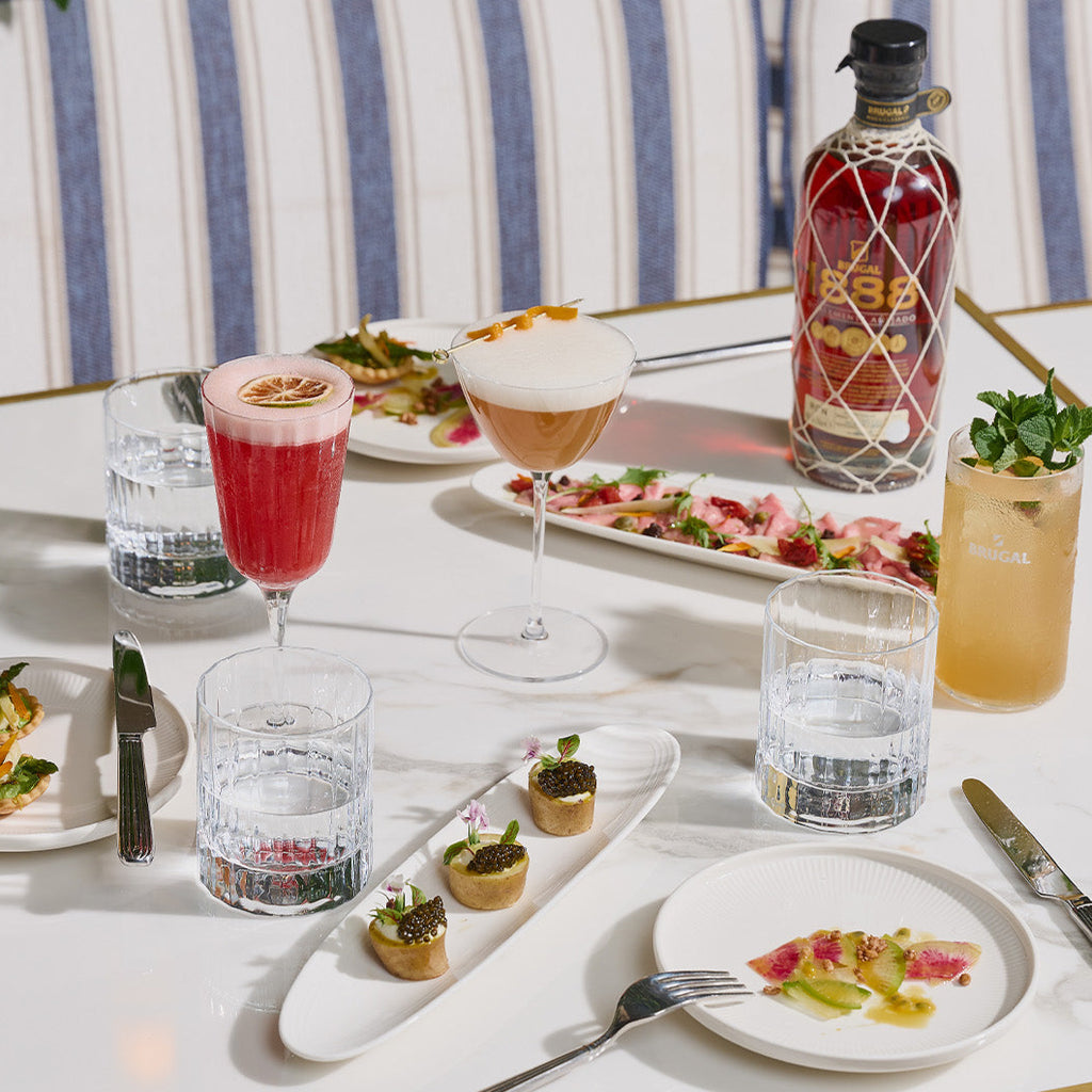 Dining table with appetizers, drinks, and a bottle of 1888 rum on a striped chair background.