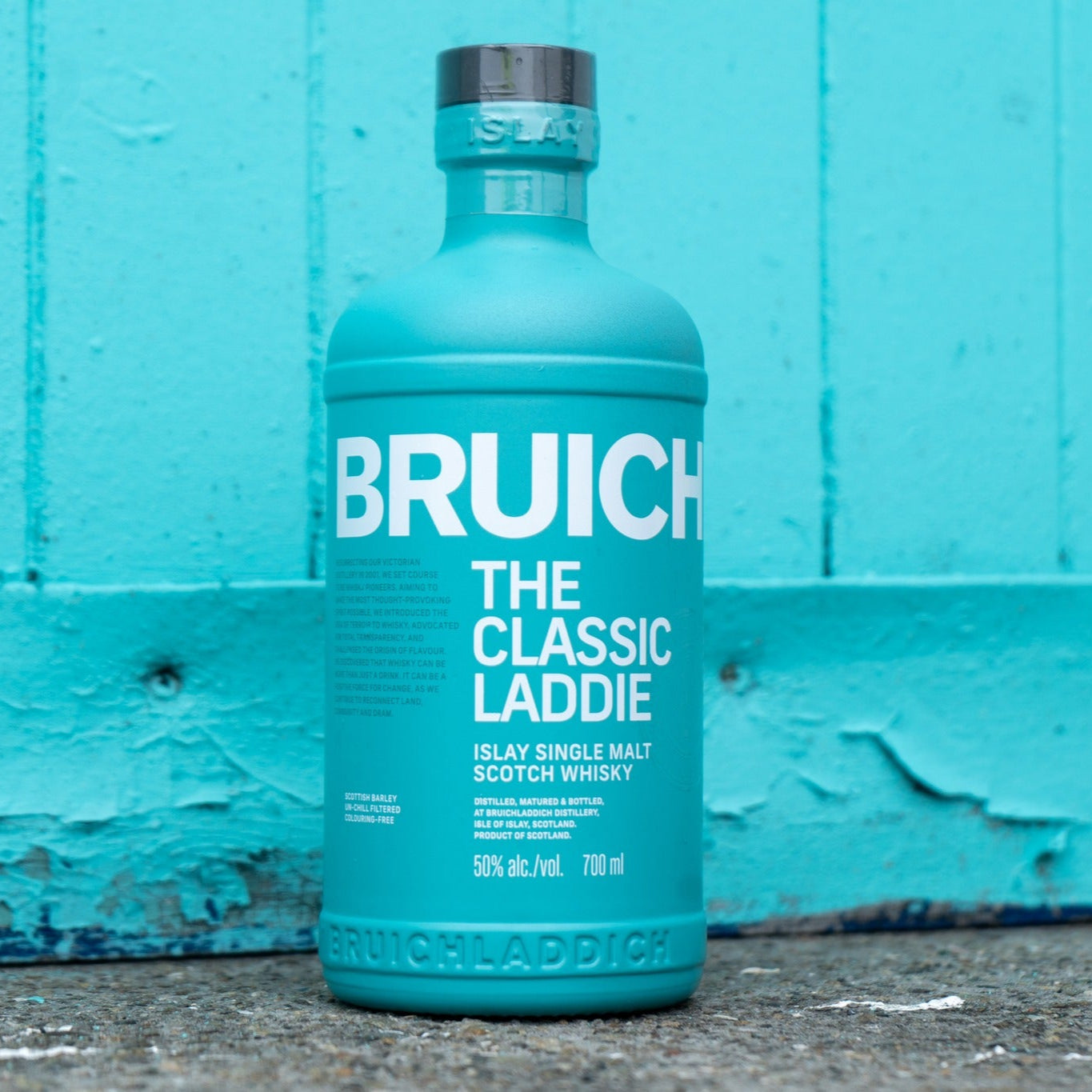 Load image into Gallery viewer, Blue Bruichladdich whisky bottle against a turquoise wall