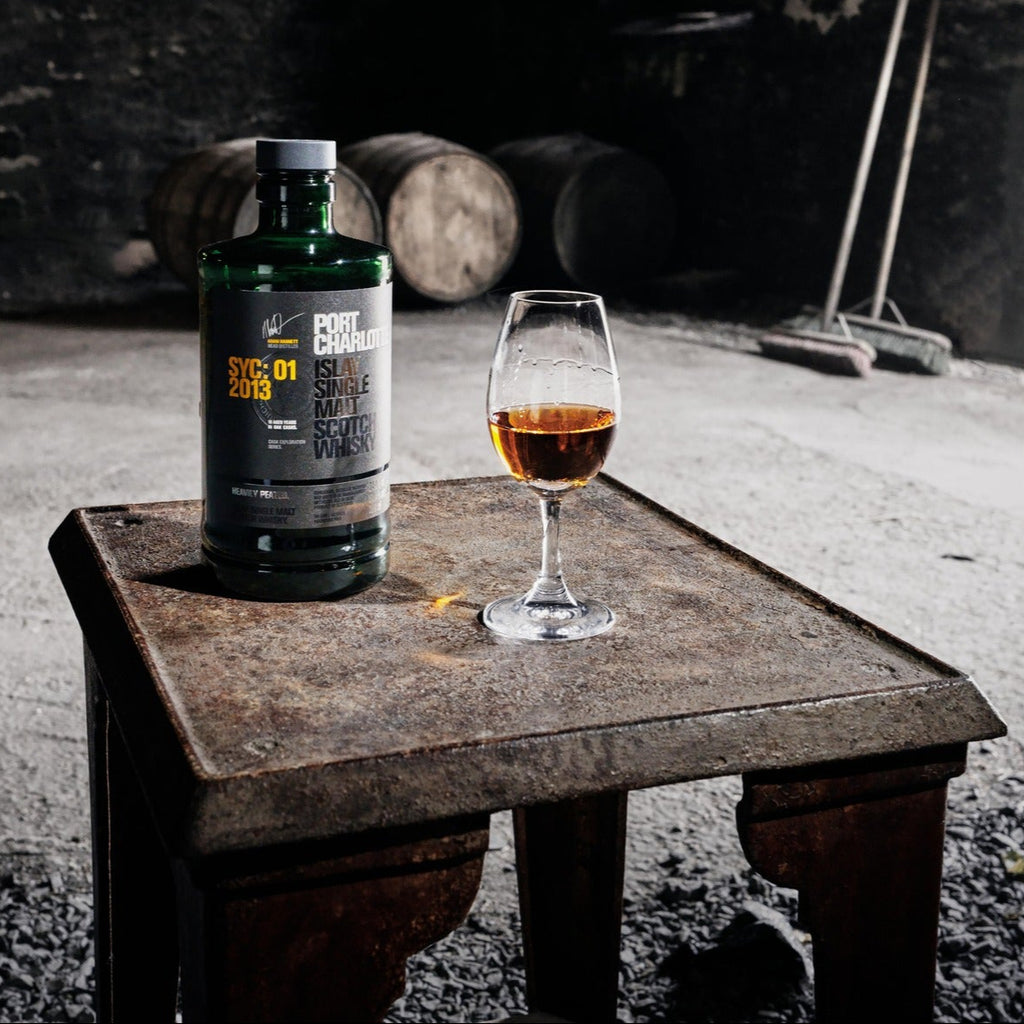 A bottle of Bruichladdich Port Charlotte 10 year old whisky and a glass of whisky on a table in a dark room