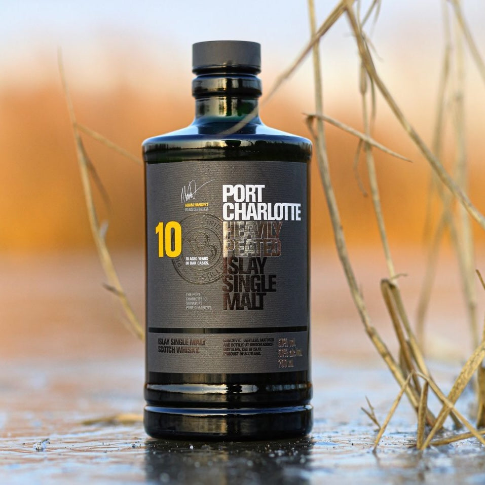 Load image into Gallery viewer,  A bottle of Bruichladdich Port Charlotte 10 year old whisky in a water puddle 