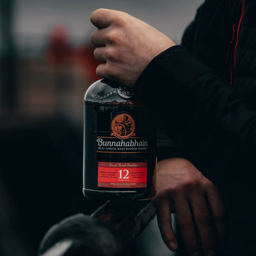 Hand holding a bottle of Bunnahabhain 12 year old whisky with a blurred background