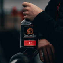 Load image into Gallery viewer, Hand holding a bottle of Bunnahabhain 12 year old whisky with a blurred background