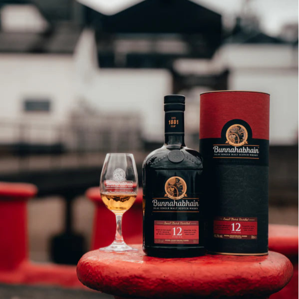 Bunnahabhain 12-year-old whisky bottle and packaging on a red surface with a blurred background