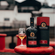 Load image into Gallery viewer, Bunnahabhain 12-year-old whisky bottle and packaging on a red surface with a blurred background