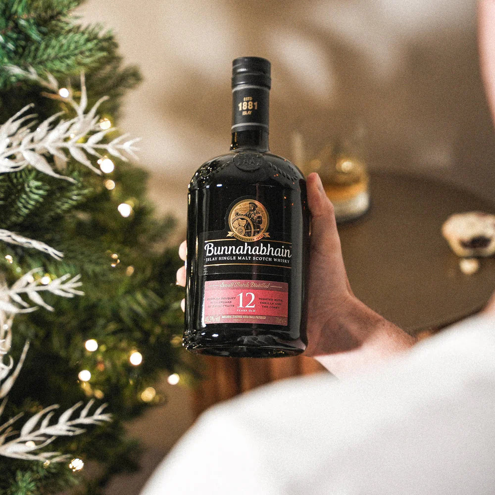 Bottle of Bunnahabhain 12 year old whisky held in front of a decorated Christmas tree.