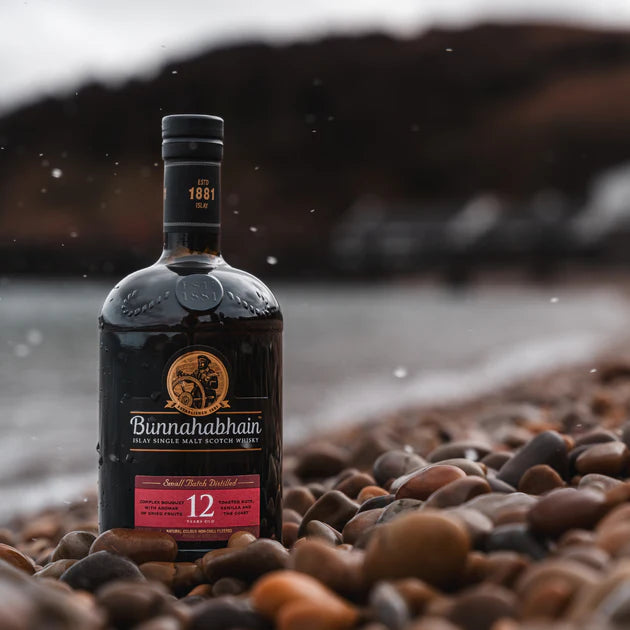 Bottle of Bunnahabhain 12 year old whisky on a pebbly beach with a blurred natural background