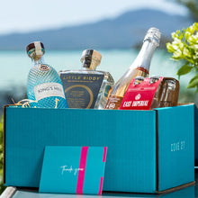 Load image into Gallery viewer, Gourmet gift box with bottles and a card on a blue surface with a blurred natural background