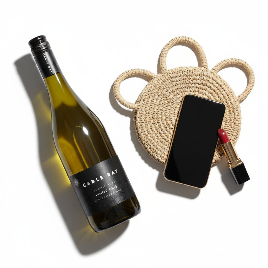 Load image into Gallery viewer, A Cable Bay Awatere Valley Pinot Gris wine bottle next to a woven phone holder with a phone and lipstick on a white background
